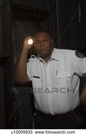 Stock Image - Security guard investigates with torch. Fotosearch