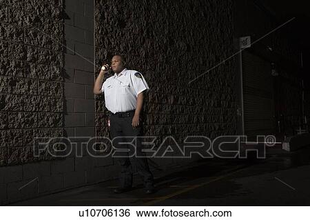 Stock Photograph - Security guard patrols at night with torch. Fotosearch