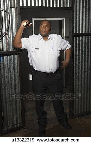 Stock Photo - Security guard stands at corrugated metal doorway with torch. Fotosearch