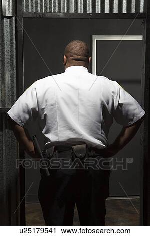 Stock Image - Security guard stands with hands on hips rear view. Fotosearch