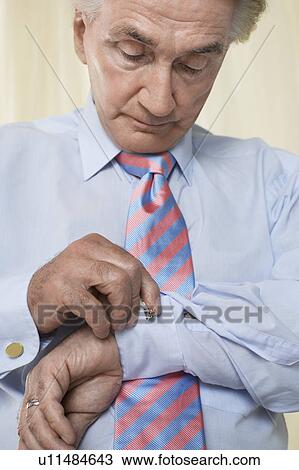 Stock Image - Senior man doing up cuff links in studio. Fotosearch