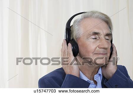 Stock Image - Senior man wearing headphones, head and shoulders, in studio. Fotosearch