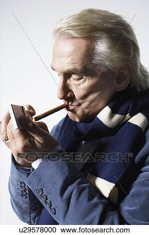 Stock Image - Senior Man wearing suit and lighting cigar in studio. Fotosearch