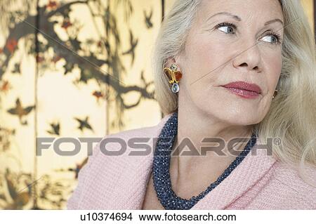 Picture - Senior woman looking over shoulder, in front of screen. Fotosearch