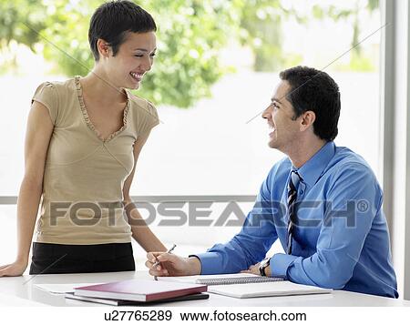 Stock Photo - Smiling businessman and businesswoman at office table talking. Fotosearch