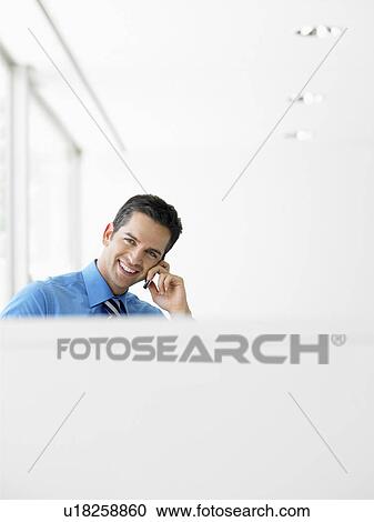 Smiling businessman in office on cell phone View Large Photo Image Stock Image - Smiling businessman in office on cell phone. Fotosearch