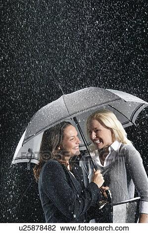 Smiling Businesswomen Standing Under Umbrella together during rain View Large Photo Image Stock Image - Smiling Businesswomen Standing Under Umbrella together during rain. Fotosearch