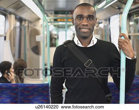 Stock Image - Smiling Commuter Standing on Train, holding bar. Fotosearch