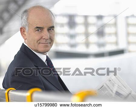 Smiling, mature Businessman Sitting on Bench with newspaper, looking over shoulder View Large Photo Image Stock Image - Smiling, mature Businessman Sitting on Bench with newspaper, looking over shoulder. Fotosearch