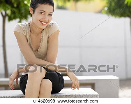 Stock Photo - Smiling woman sitting on bench in plaza, portrait. Fotosearch
