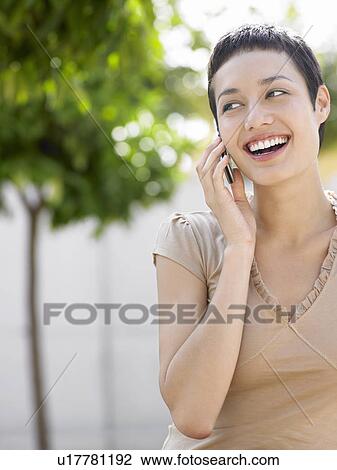 Stock Image - Smiling young woman on cell phone in plaza courtyard. Fotosearch