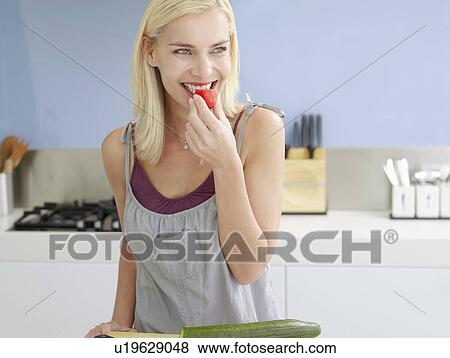 Smiling, young woman Snacking on cherry tomato in Kitchen View Large Photo Image Stock Photo - Smiling, young woman Snacking on cherry tomato in Kitchen. Fotosearch