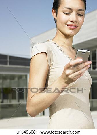 Stock Image - Smiling young woman standing in plaza sending text message. Fotosearch