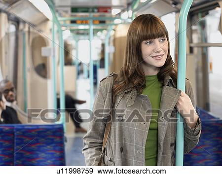 Smiling, Young Woman Standing on Commuter Train, holding bar View Large Photo Image Stock Photo - Smiling, Young Woman Standing on Commuter Train, holding bar. Fotosearch