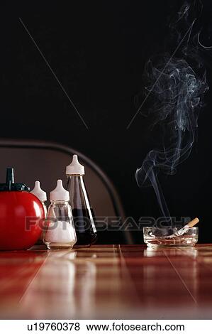 Stock Photo - Smoking cigarette in ashtray on table with condiments. Fotosearch