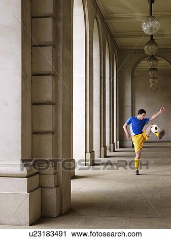 Stock Image - Soccer player kicking ball in portico. Fotosearch