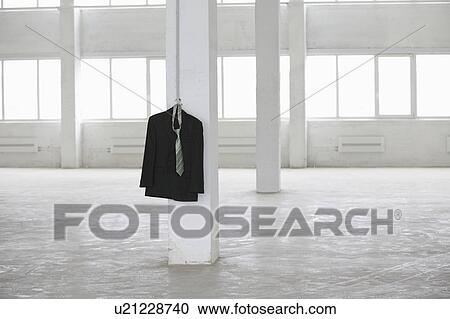 Stock Image - Suit jacket hangs on pillar in empty warehouse. Fotosearch