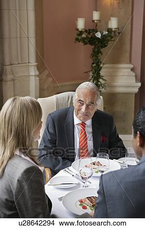 Picture - Three business people sitting at restaurant table, talking. Fotosearch