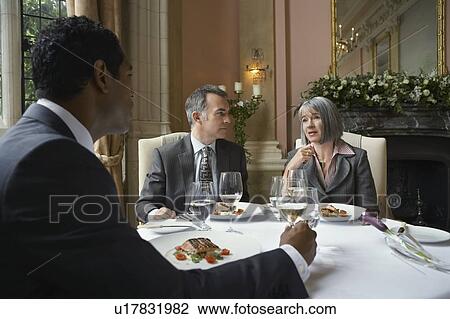 Stock Image - Three business people sitting at restaurant table, talking. Fotosearch