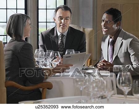Three business people sitting at restaurant table, woman holding documents View Large Photo Image Stock Image - Three business people sitting at restaurant table, woman holding documents. Fotosearch