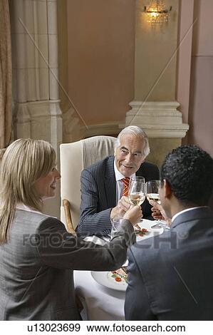 Three business people sitting at restaurant table, toasting View Large Photo Image Stock Photo - Three business people sitting at restaurant table, toasting. Fotosearch