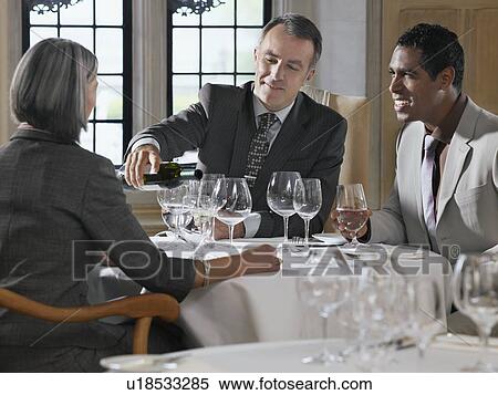 Three business people sitting at restaurant table, man pouring wine View Large Photo Image Stock Photography - Three business people sitting at restaurant table, man pouring wine. Fotosearch