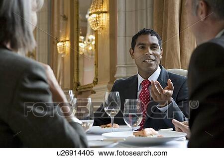 Three business people sitting at restaurant table, talking View Large Photo Image Stock Photography - Three business people sitting at restaurant table, talking. Fotosearch