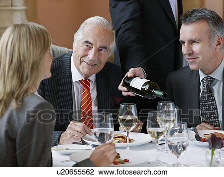 Three business people talking at restaurant table, waiter serving wine View Large Photo Image Stock Image - Three business people talking at restaurant table, waiter serving wine. Fotosearch