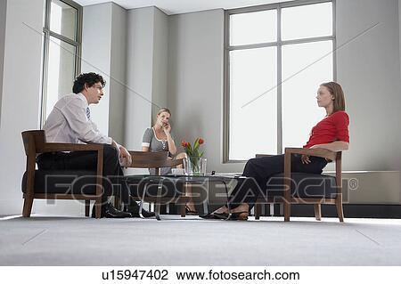 Stock Image - Three businesspeople sitting at table talking, low angle view. Fotosearch