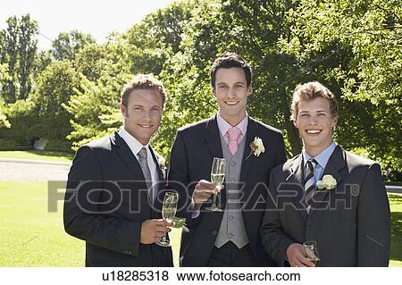 Stock Photo - Three men in garden, wearing full suits, holding wineglasses, portrait. Fotosearch