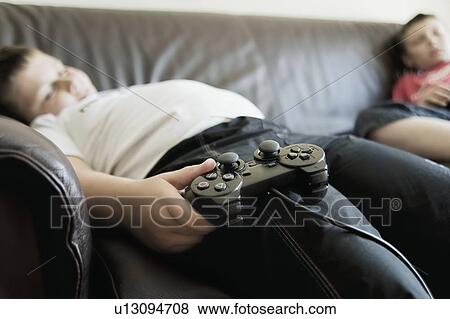 Two boys sleep on sofa holding games consoles View Large Photo Image Stock Photo - Two boys sleep on sofa holding games consoles. Fotosearch