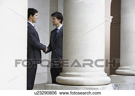 Two business men shaking hands outside building by pillar View Large Photo Image Stock Photograph - Two business men shaking hands outside building by pillar. Fotosearch