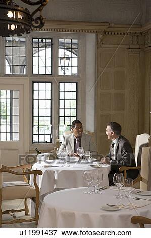 Stock Photo - Two business men sitting at restaurant table talking. Fotosearch
