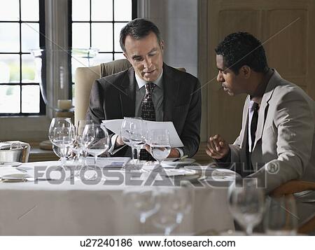 Two business men sitting at restaurant table analyzing documents View Large Photo Image Stock Photograph - Two business men sitting at restaurant table analyzing documents. Fotosearch