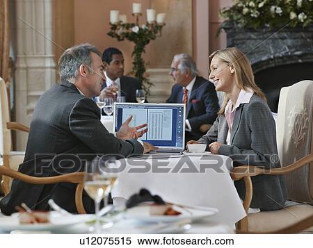 Stock Photography - Two business people having conversation at restaurant table with laptop. Fotosearch