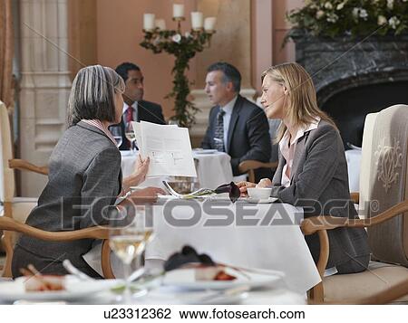 Two business women looking at documents at restaurant table, men in background View Large Photo Image Stock Image - Two business women looking at documents at restaurant table, men in background. Fotosearch