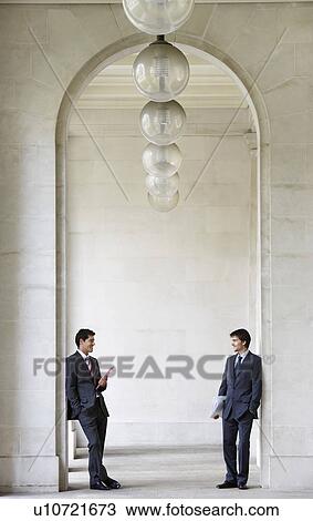 Stock Image - Two Businessmen outside building in archway talking. Fotosearch