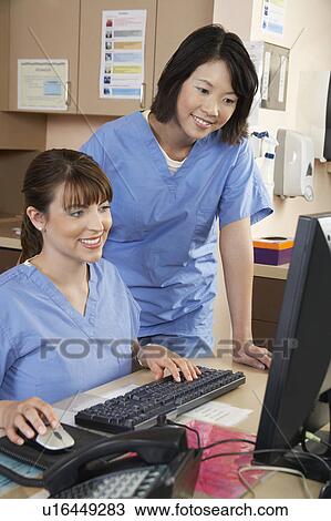 Stock Image - Two female nurses working on computer in doctor's office. Fotosearch