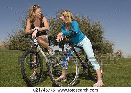 Stock Photography - Two friends lean on their bikes talking. Fotosearch