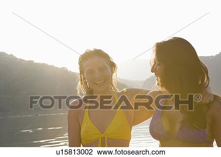 Stock Image - Two friends stand laughing in swimwear at dawn. Fotosearch