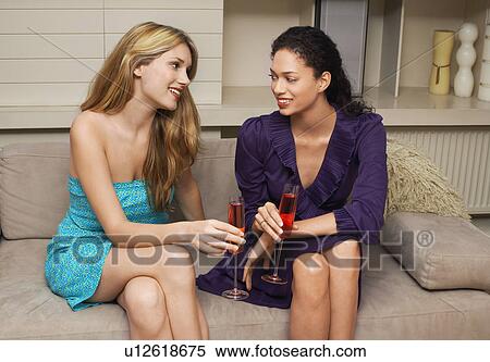 Stock Photography - Two girls Drinking on Sofa. Fotosearch