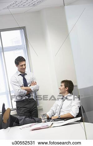 Stock Image - Two happy businessmen relaxing and talking in office. Fotosearch