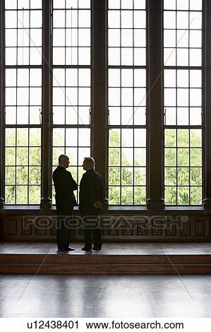 Stock Image - Two Men Conversing by tall windows. Fotosearch