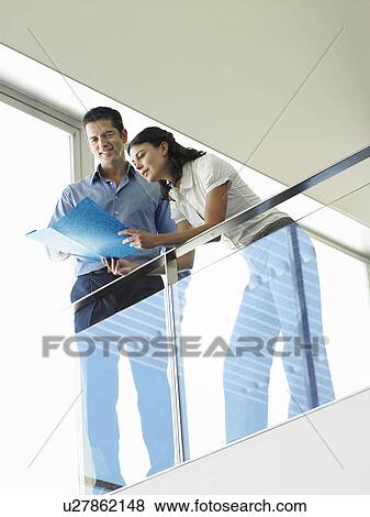 Stock Photo - Two office Workers Reading Document on office balcony, view from below. Fotosearch
