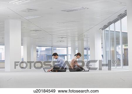 Two office workers sitting back to back, using laptops, on floor of empty office space View Large Photo Image Stock Photo - Two office workers sitting back to back, using laptops, on floor of empty office space. Fotosearch