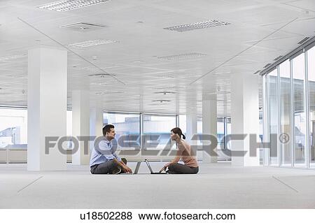 Two office workers sitting face to face, using laptops, on floor of empty office space View Large Photo Image Stock Photo - Two office workers sitting face to face, using laptops, on floor of empty office space. Fotosearch