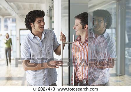Stock Image - Two office workers talking at glass door in office. Fotosearch