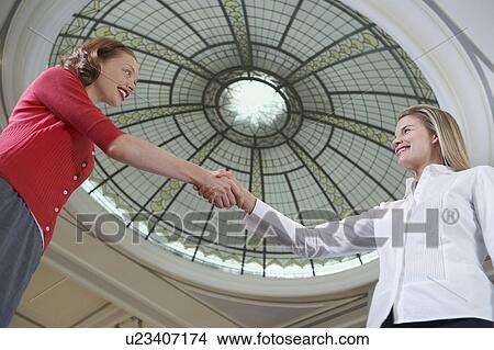 Picture - Two women shaking hands under dome, low angle view. Fotosearch
