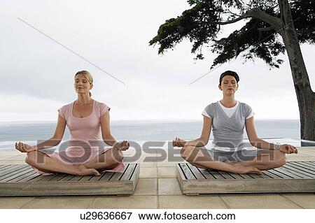 Stock Photo - Two women sitting in yoga positions on terrace. Fotosearch