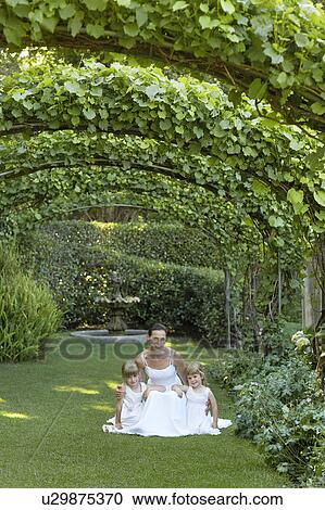 Two young girls and mid adult bride squatting under ivy arches, portrait View Large Photo Image Stock Image - Two young girls and mid adult bride squatting under ivy arches, portrait. Fotosearch